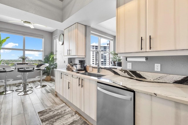 kitchen with light stone counters, light wood-style flooring, a sink, dishwasher, and baseboards