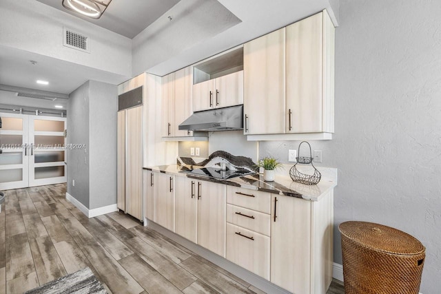 kitchen with cream cabinets, light brown cabinets, light stone counters, and hardwood / wood-style floors