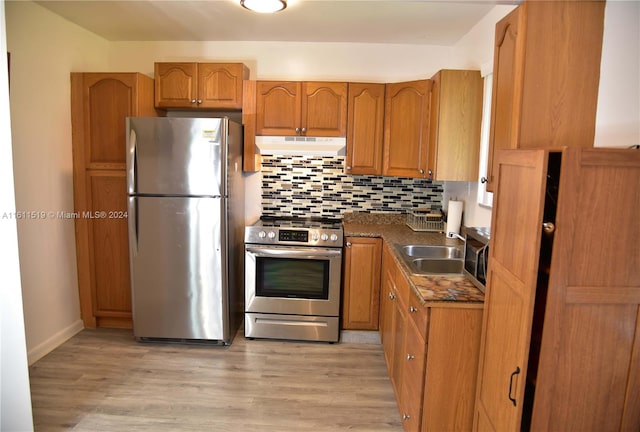 kitchen featuring appliances with stainless steel finishes, light wood-type flooring, tasteful backsplash, and dark stone counters