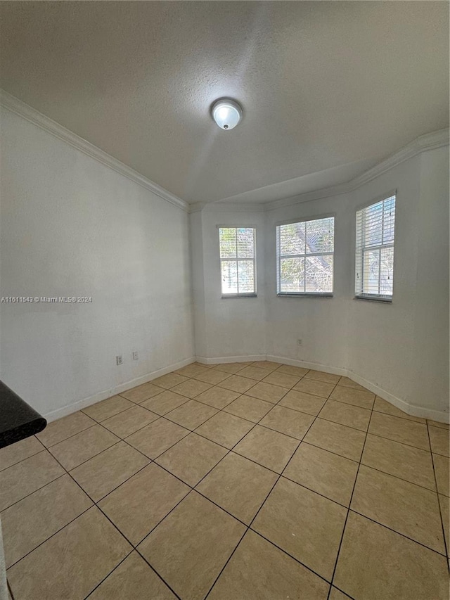 tiled empty room featuring crown molding and a textured ceiling