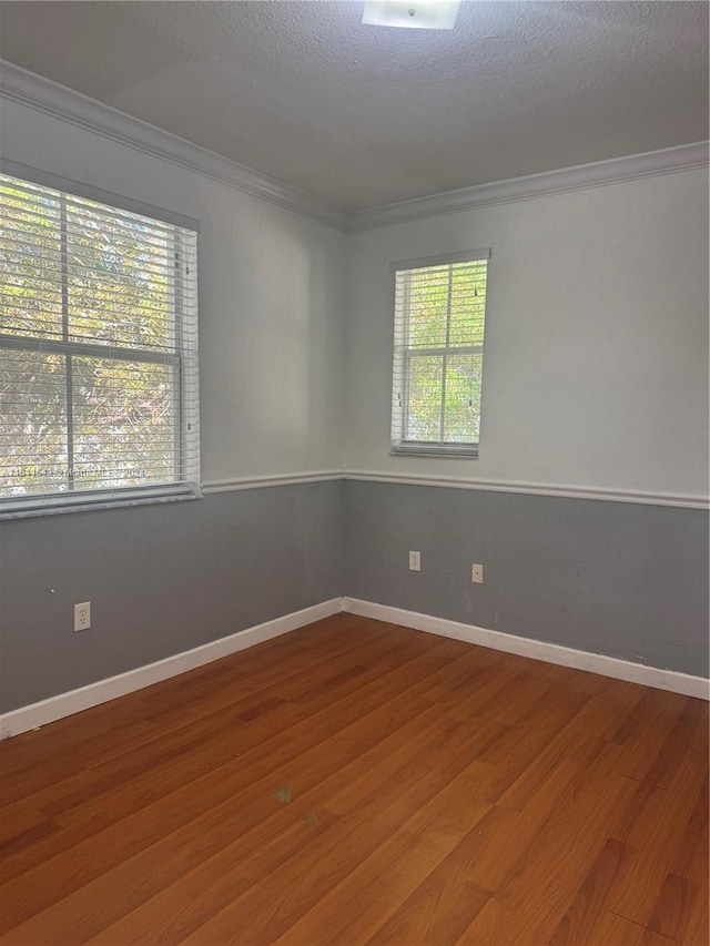 empty room featuring plenty of natural light, ornamental molding, a textured ceiling, and hardwood / wood-style flooring