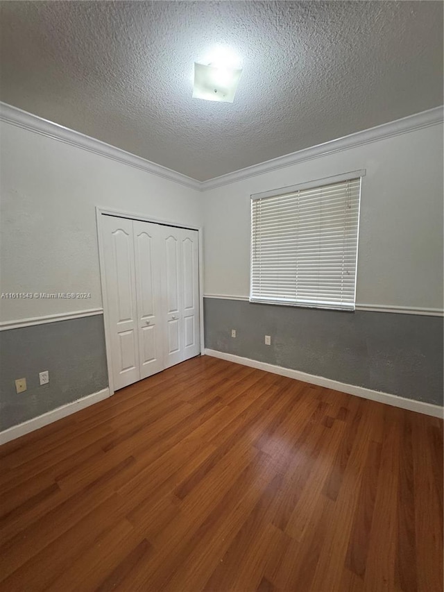 unfurnished bedroom featuring hardwood / wood-style floors, a textured ceiling, a closet, and crown molding