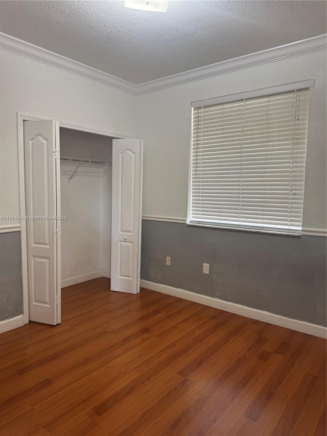 unfurnished bedroom with a closet, hardwood / wood-style floors, a textured ceiling, and ornamental molding