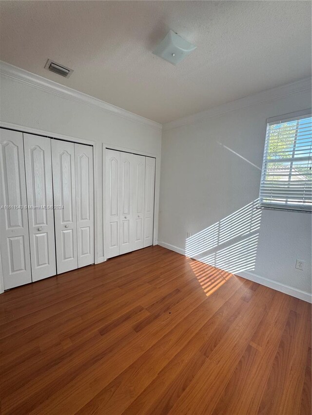 unfurnished bedroom with wood-type flooring, a textured ceiling, multiple closets, and crown molding