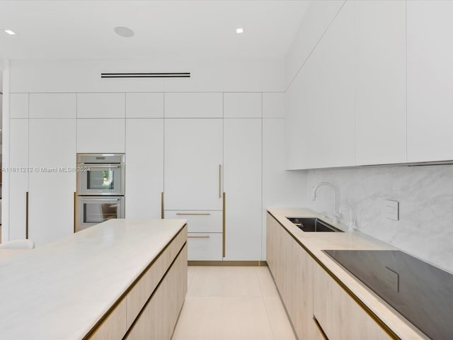 kitchen with stainless steel double oven, backsplash, light tile floors, sink, and white cabinets