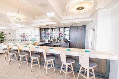 bar featuring coffered ceiling, gray cabinetry, light hardwood / wood-style floors, and decorative light fixtures