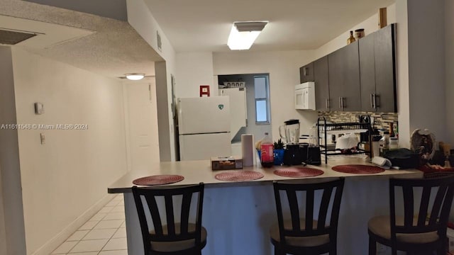 kitchen featuring a kitchen breakfast bar, white appliances, kitchen peninsula, tasteful backsplash, and light tile floors