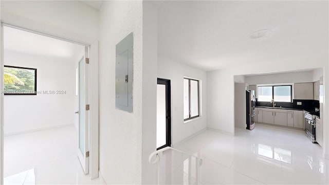 corridor featuring electric panel, sink, light tile patterned floors, and a wealth of natural light