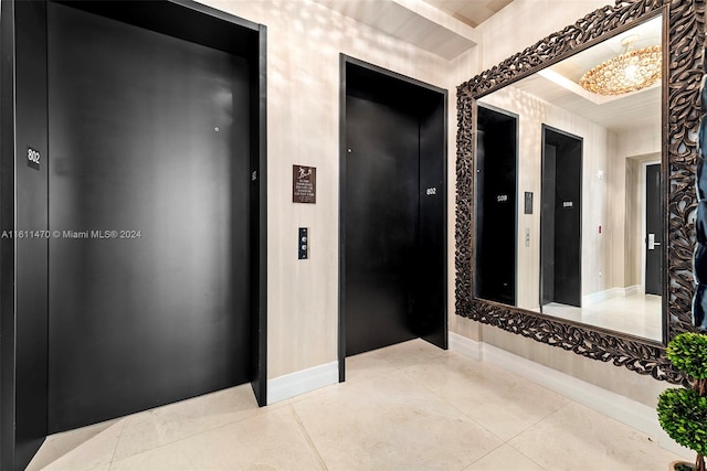 hallway with tile floors, elevator, and a chandelier