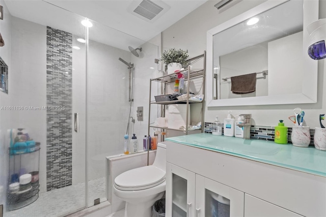 bathroom with vanity, toilet, a shower with shower door, and backsplash