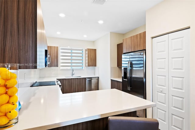 kitchen with kitchen peninsula, tasteful backsplash, a breakfast bar area, appliances with stainless steel finishes, and sink