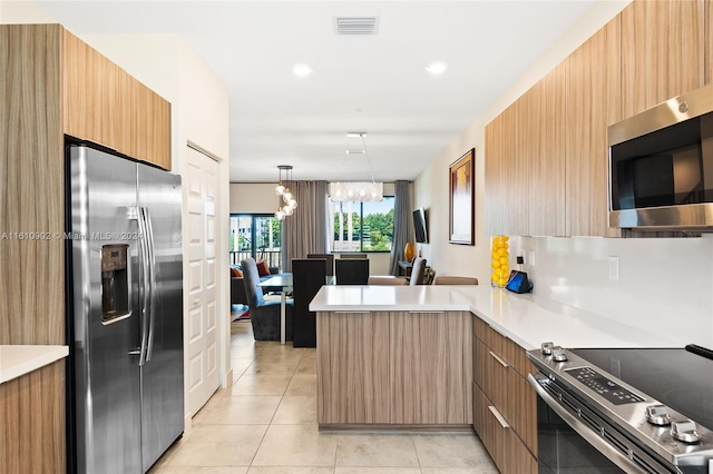 kitchen with an inviting chandelier, appliances with stainless steel finishes, kitchen peninsula, pendant lighting, and light tile floors