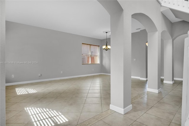 tiled spare room featuring a notable chandelier