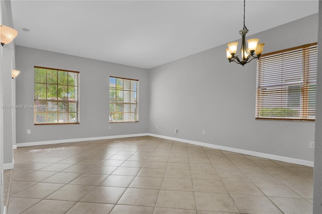 tiled spare room with an inviting chandelier