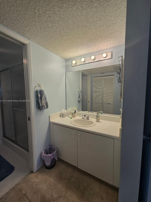 bathroom with vanity, a shower with shower door, and a textured ceiling