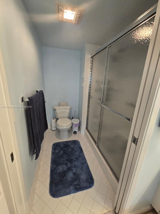 bathroom with tile patterned flooring, toilet, and a shower with door