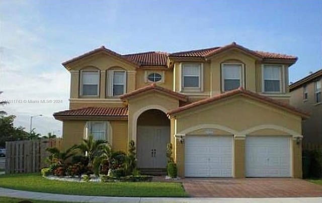 mediterranean / spanish house featuring decorative driveway, stucco siding, fence, a garage, and a tiled roof