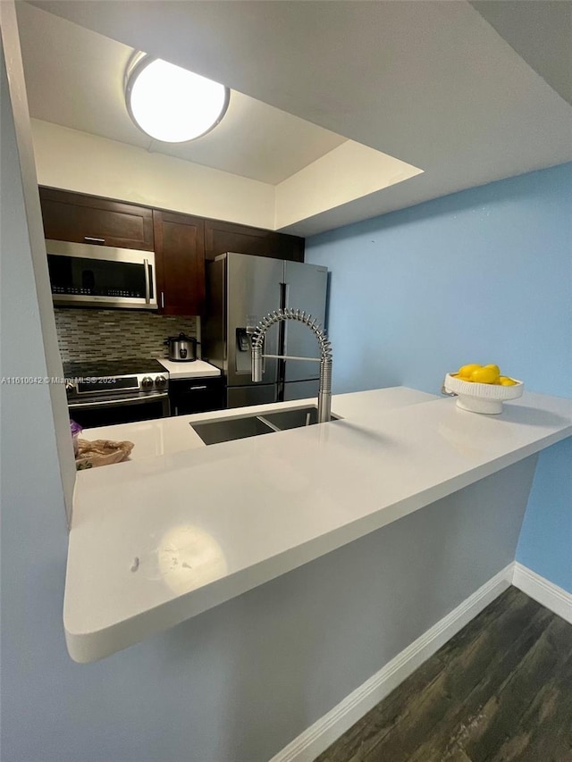 kitchen with backsplash, a tray ceiling, dark brown cabinetry, dark wood-type flooring, and appliances with stainless steel finishes