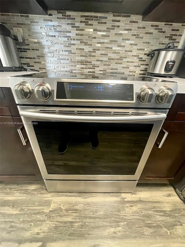 details with backsplash, stainless steel electric range oven, oven, light wood-type flooring, and dark brown cabinets