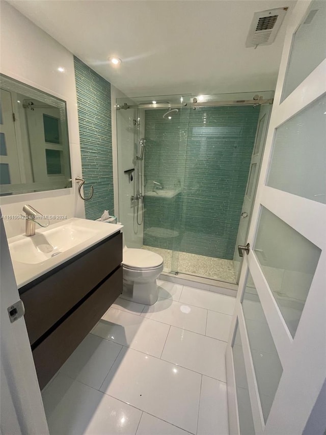 bathroom with toilet, tile patterned floors, vanity, and a shower with shower door