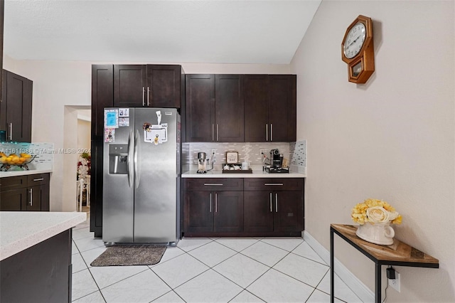 kitchen with stainless steel refrigerator with ice dispenser, dark brown cabinetry, light tile flooring, and backsplash