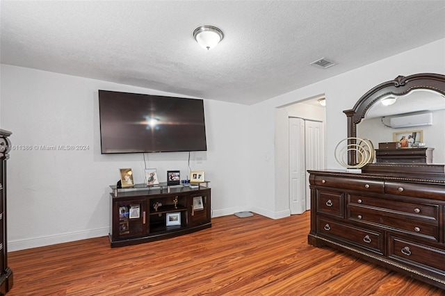 living room with a wall unit AC, a textured ceiling, and hardwood / wood-style floors