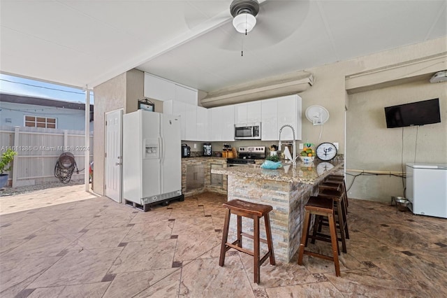 kitchen featuring ceiling fan, stainless steel appliances, light tile floors, a kitchen bar, and white cabinetry