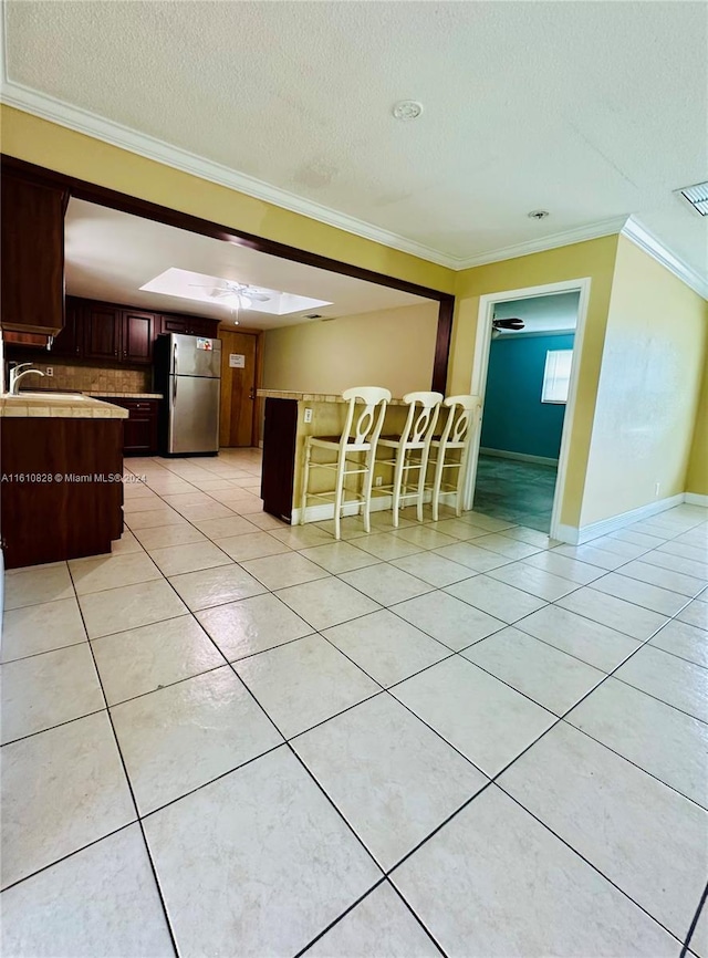 kitchen with crown molding, light tile patterned flooring, a textured ceiling, stainless steel refrigerator, and a skylight