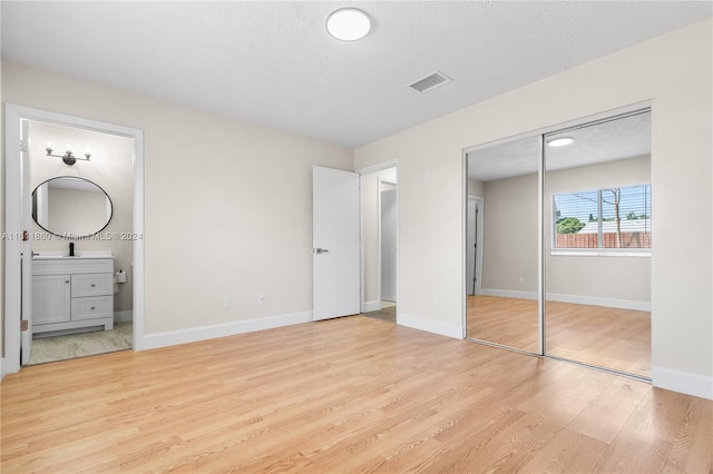 unfurnished bedroom featuring a textured ceiling, light hardwood / wood-style floors, and ensuite bath