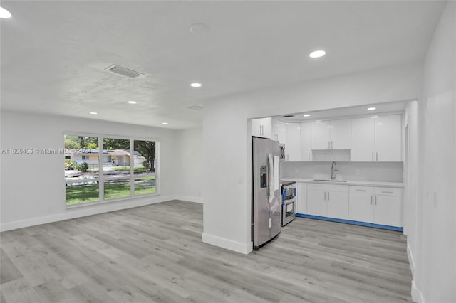 kitchen with appliances with stainless steel finishes, tasteful backsplash, white cabinets, sink, and light hardwood / wood-style floors