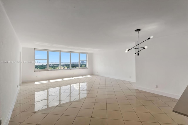 empty room featuring a notable chandelier, light tile patterned floors, and baseboards