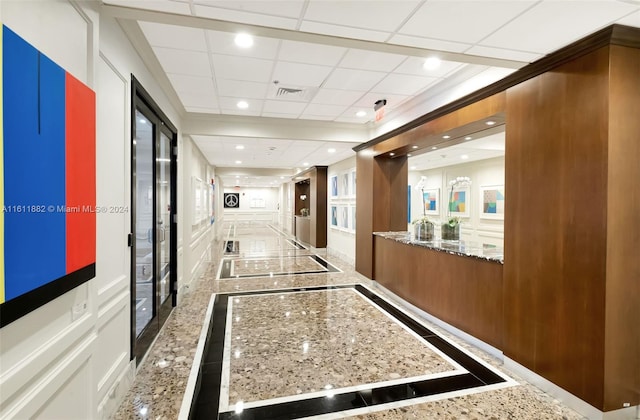 hallway with a paneled ceiling and ornamental molding