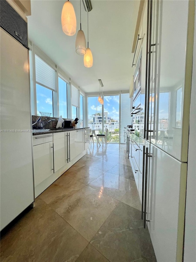 kitchen featuring built in appliances, hanging light fixtures, and white cabinets