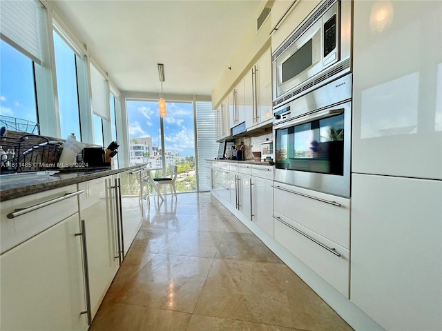 kitchen featuring appliances with stainless steel finishes, expansive windows, white cabinets, and decorative light fixtures