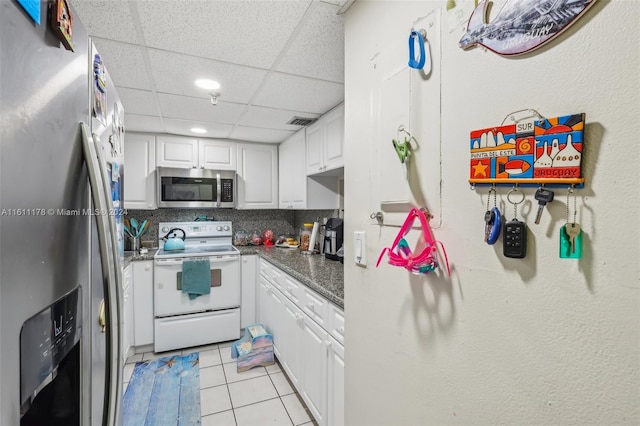 kitchen with appliances with stainless steel finishes, white cabinetry, backsplash, light tile patterned floors, and a paneled ceiling