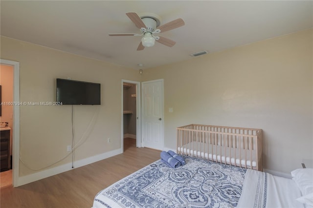 bedroom featuring a spacious closet, a closet, wood-type flooring, and ceiling fan