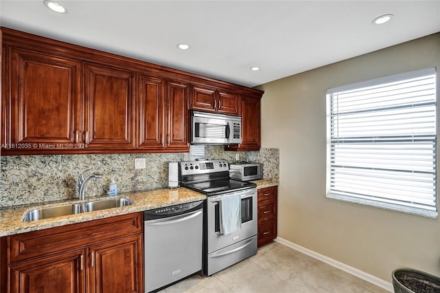 kitchen featuring light stone countertops, appliances with stainless steel finishes, backsplash, sink, and light tile floors