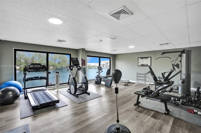 gym with a water view, hardwood / wood-style flooring, and a drop ceiling