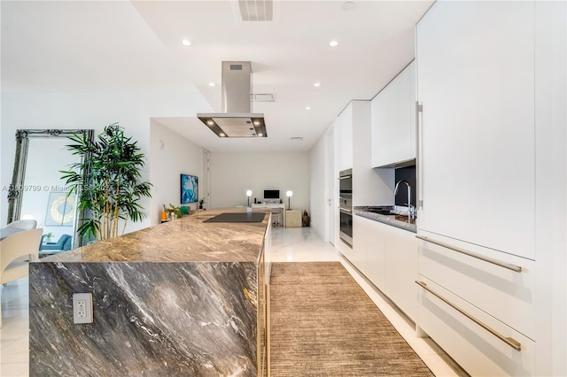 kitchen with sink, dark stone countertops, island exhaust hood, oven, and white cabinets