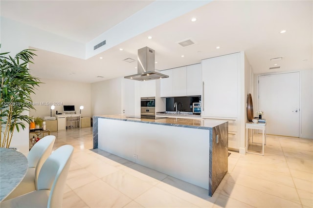 kitchen with island exhaust hood, cooktop, sink, dark stone countertops, and white cabinets