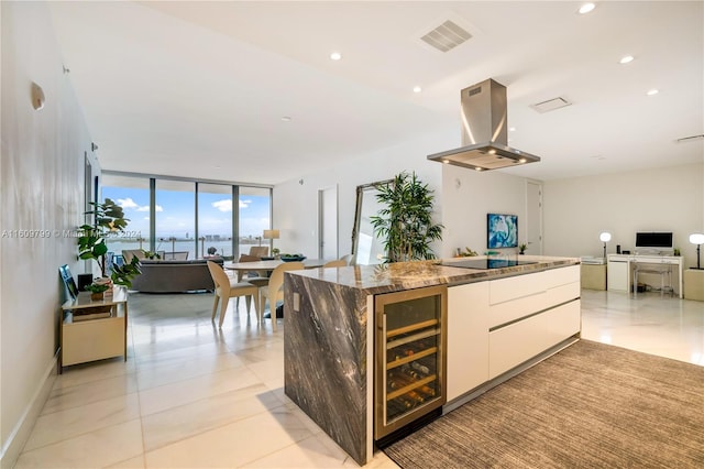 kitchen featuring light stone countertops, island range hood, a wall of windows, white cabinets, and wine cooler