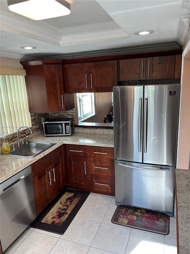 kitchen featuring ornamental molding, stainless steel appliances, a tray ceiling, sink, and light tile patterned floors