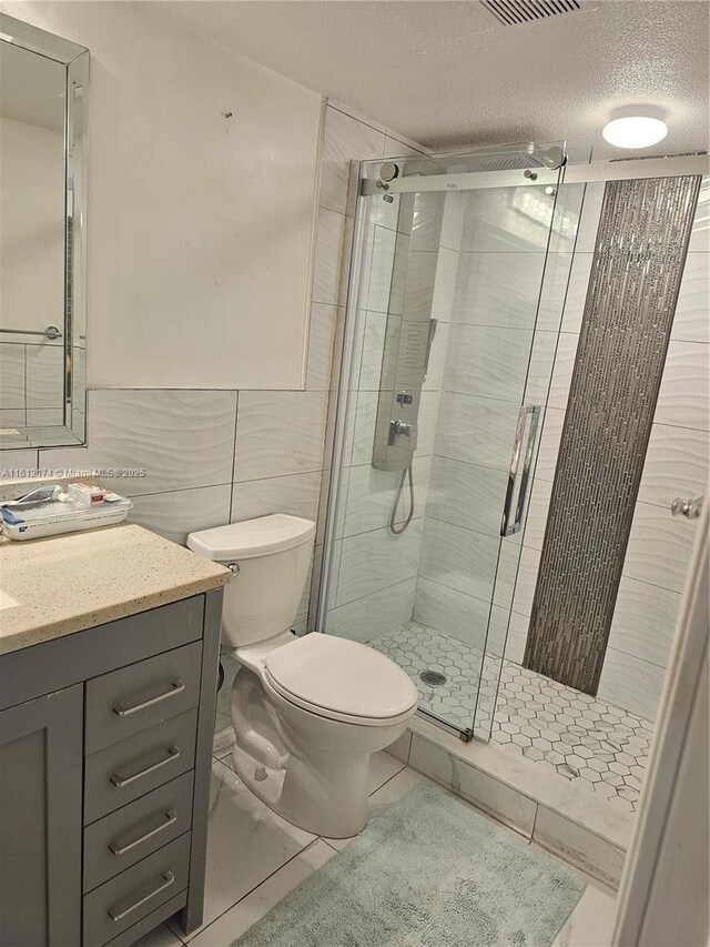 bathroom with vanity, a shower with door, tile patterned flooring, a textured ceiling, and tile walls