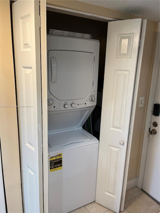 clothes washing area with stacked washer / dryer, light tile patterned floors, and a textured ceiling