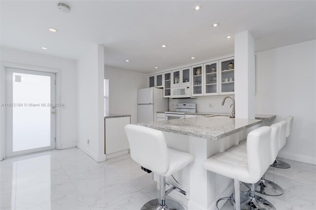 kitchen featuring white cabinetry, white appliances, kitchen peninsula, sink, and light tile floors