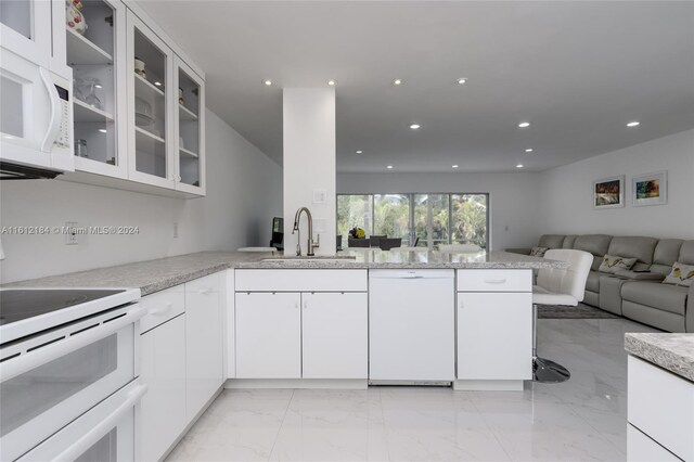 kitchen featuring kitchen peninsula, white appliances, light tile floors, sink, and white cabinets