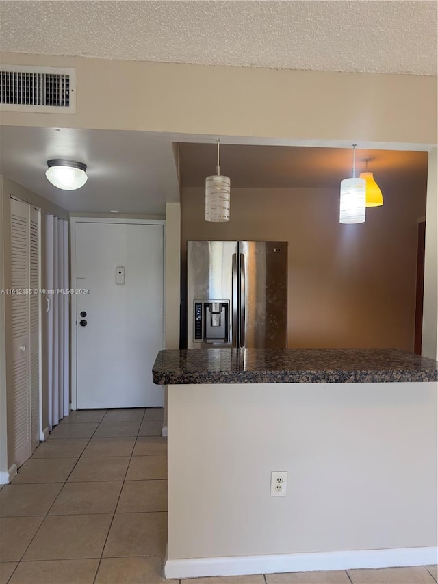 kitchen with pendant lighting, a textured ceiling, dark tile patterned flooring, and stainless steel fridge with ice dispenser