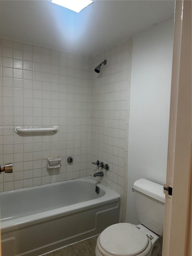 bathroom featuring tile patterned flooring, tiled shower / bath combo, and toilet