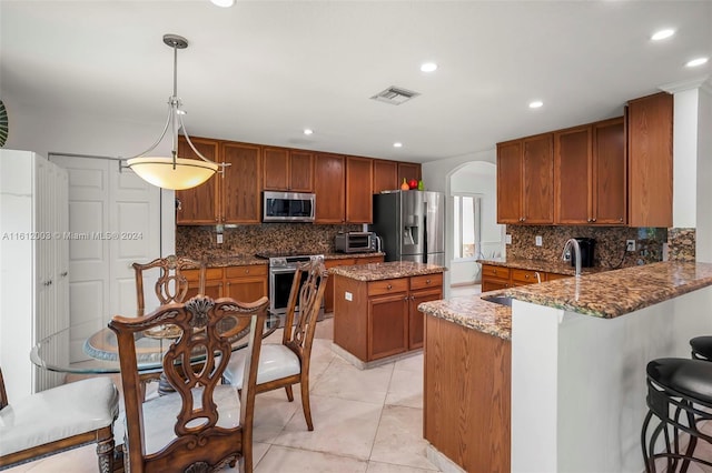 kitchen featuring light stone counters, backsplash, appliances with stainless steel finishes, decorative light fixtures, and kitchen peninsula