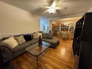 living area with ceiling fan with notable chandelier and wood finished floors